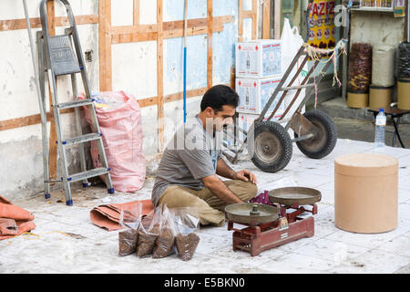 Local Arab man sitting on pavement with scales, intently weighing out bags of spices, Deira, Dubai, UAE Stock Photo