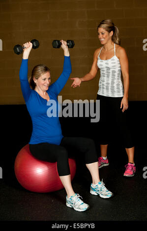 A young pregnant woman working out with an atletic female trainer at the gym. Stock Photo