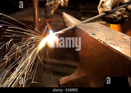 A metal fabricator utilizing a torch to heat up a piece of metal in order to shape it. Stock Photo