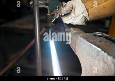 A metal fabricator utilizing a torch to heat up a piece of metal in order to shape it. Stock Photo