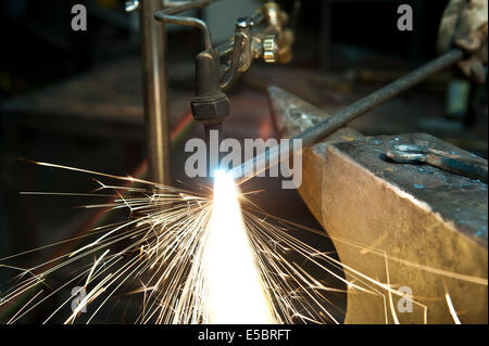 A metal fabricator utilizing a torch to heat up a piece of metal in order to shape it. Stock Photo