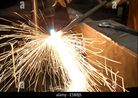 A metal fabricator utilizing a torch to heat up a piece of metal in order to shape it. Stock Photo