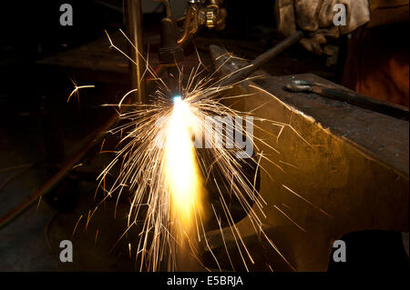 A metal fabricator utilizing a torch to heat up a piece of metal in order to shape it. Stock Photo