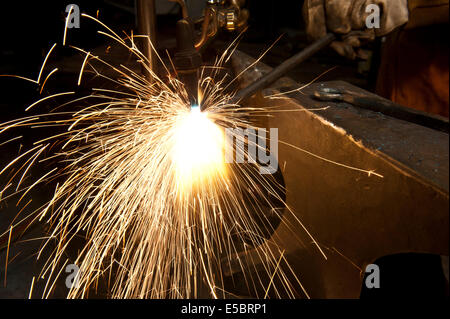 A metal fabricator utilizing a torch to heat up a piece of metal in order to shape it. Stock Photo