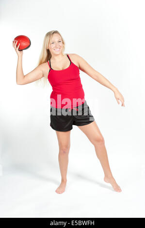 A young female model wearing a red t-shirt with black shorts ready to throw a red and black football on a white background. Stock Photo