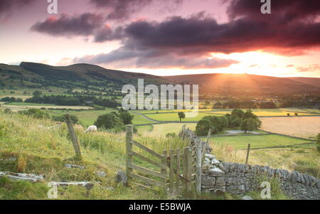 Peak District, Derbyshire, UK. 27 July 2014.  A peachy sunrise lights up dark clouds scudding over the Hope Valley near Castleton in the Peak District National Park on a fine, breezy morning.  The recent very warm weather is forecast to continue with variable cloud, showers and longer spells of rain affecting parts of the UK during National Parks Week that begins tomorrow (Mon 28 July) and runs until Sun 3 August.  The Peak District became Britain’s first national park in 1951. Credit:  Matthew Taylor/Alamy Live News Stock Photo