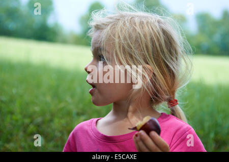 Portrait of child blond Girl eating a plum on meadow Stock Photo