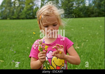 Little child blond girl on the meadow holding flowers Stock Photo