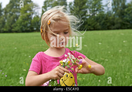 Little child blond girl on the meadow holding flowers Stock Photo