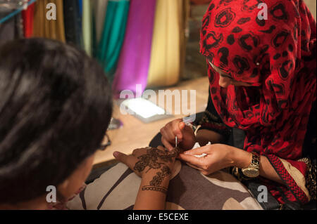 Upper Tooting Road, Tooting, London, UK. 28th July 2014. Hundreds of Muslims celebrate the beginning of Eid ul-Fitr at midnight in Tooting Bec, south west London. Upper Tooting Road was crowded with people eager to eat snacks, buy clothes or dance in the street. Pictured: A woman applies henna to a customer's hand. Credit:  Lee Thomas/Alamy Live News Stock Photo