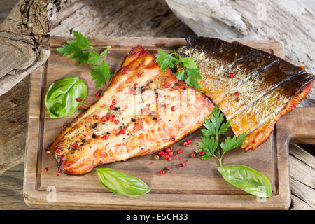 Closeup horizontal view of smoked salmon fillets with seasoning inside of drift wood on serving board Stock Photo