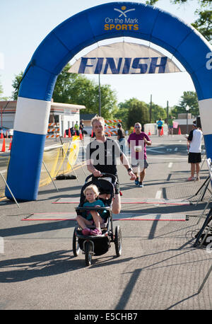 Man in 5K or 10K marathon race crossing finish line with baby in stroller Stock Photo