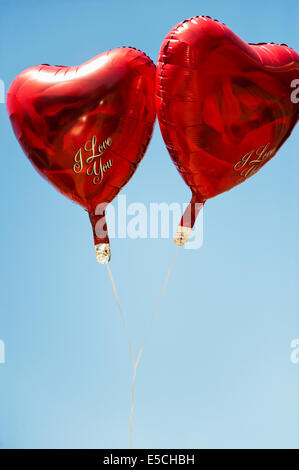Two mylar heart shaped helium balloons silhouetted against a bright blue sky Stock Photo