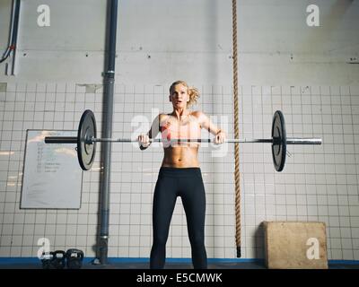 Young strong woman practices cross fit in a gym. Fit female holding a barbell with weights for crossfit. Stock Photo