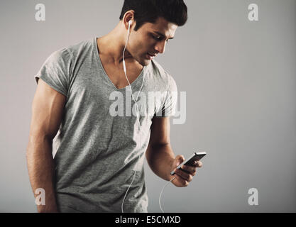 Portrait of casual young man with cell phone and headphones listening to music on grey background. Enjoying listening music.