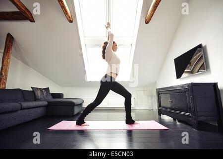 Full length image of woman standing on exercise mat with arms outstretched doing yoga at home. Healthy caucasian female model ex Stock Photo