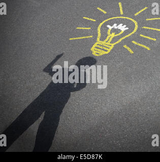 Childhood imagination and child creativity concept as the shadow of an inspired boy with a lightbulb chalk drawing on city asphalt as a symbol of inspiration and creative learning or back to school ideas. Stock Photo