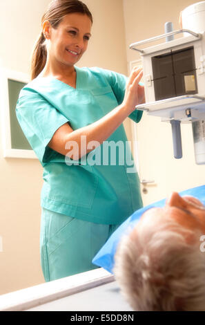 Senior man in 60s undergoing x-ray scan with smiling female doctor at the scanner machine. Stock Photo