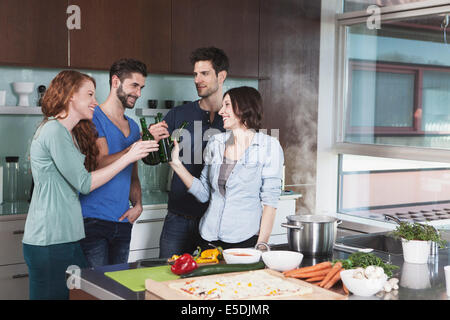 Portrait of four friends toasting with beer bottles in a kitchen Stock Photo