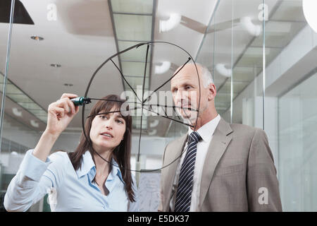 Germany, Munich, Businesswoman in office, drawing chart on glass pane Stock Photo