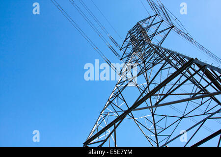 closeup under view of towering steel pylon supporting electric power cables on blue sky Stock Photo