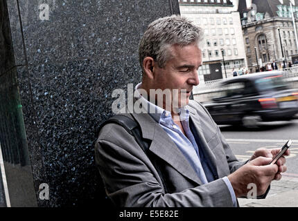 Mature businessman using an iPhone in London Southbank with blurred traditional London black cab passing in background Stock Photo
