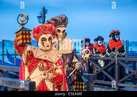 Harlequin costumed couple join other Carnival revelers on the gondolas docks along the waterfront of Venice. Stock Photo