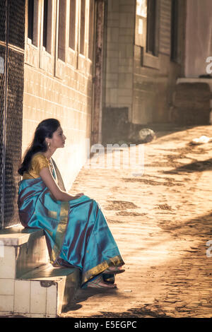 A young woman in a saree sitting on a step on a cobbled street in old Mumbai, India Stock Photo