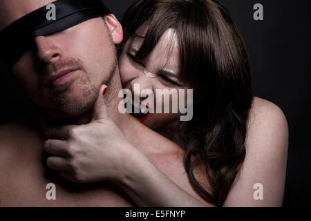 Female vampire with red lips bites man in the neck Stock Photo