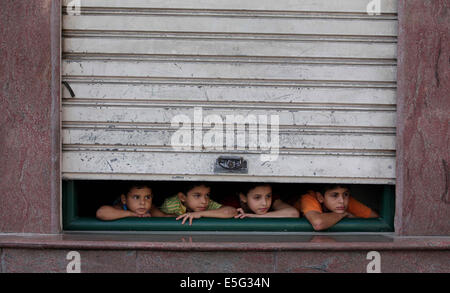 July 30, 2014 - Gaza City, Gaza Strip, Palestinian Territory - Palestinian children look through a store shutter at ambulances transporting casualties during Israeli offensive, in Gaza City July 30, 2014. Israeli strikes near a market in the eastern Gaza Strip killed 15 Palestinians on Wednesday, the local health ministry said. Residents said that Israeli shelling and two missiles from the air hit the area in Shejaia, on the fringes of the city of Gaza. Ashraf al-Qidra, spokesman of the Gaza Health Ministry, said 160 people were also wounded. An Israeli military spokeswoman said she was checki Stock Photo