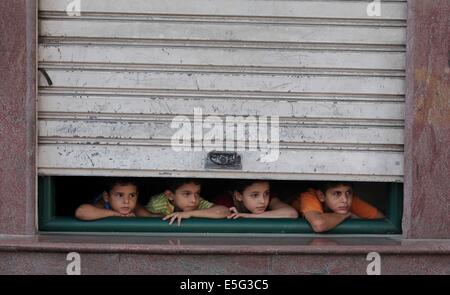 July 30, 2014 - Gaza City, Gaza Strip, Palestinian Territory - Palestinian children look through a store shutter at ambulances transporting casualties during Israeli offensive, in Gaza City July 30, 2014. Israeli strikes near a market in the eastern Gaza Strip killed 15 Palestinians on Wednesday, the local health ministry said. Residents said that Israeli shelling and two missiles from the air hit the area in Shejaia, on the fringes of the city of Gaza. Ashraf al-Qidra, spokesman of the Gaza Health Ministry, said 160 people were also wounded. An Israeli military spokeswoman said she was checki Stock Photo