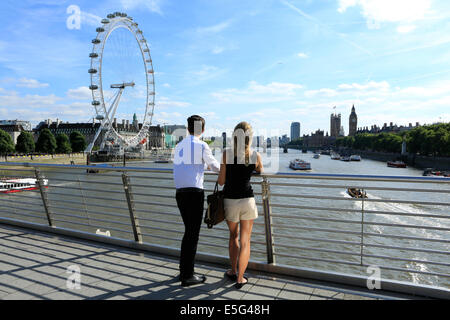 A young couple looking at the Houses of Parliament, Thames and London Eye from Hungerford Bridge Stock Photo