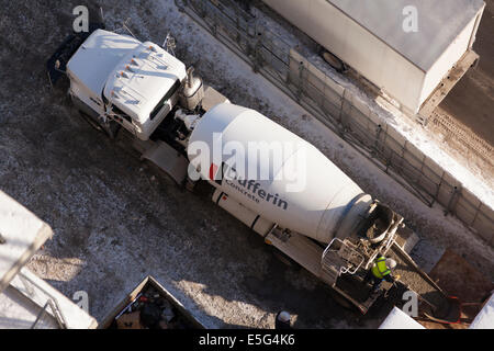 A cement mixer truck dumping a load of fresh concrete with a worker overseeing the operation. Taken from overhead in Toronto. Stock Photo