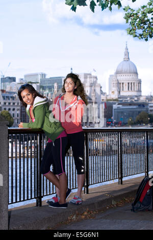 Two young women leaning against a railing on the South Bank of the Thames, London, England Stock Photo