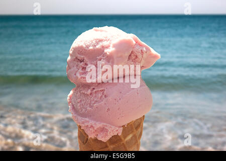 A delicious close up of a 2 scoop strawberry ice cream in a cone. At a sunny beach by the sea side. Stock Photo