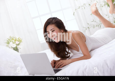 Young lady using laptop on bed Stock Photo