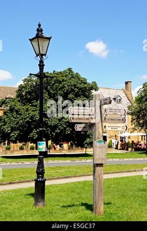 Traditional black streetlight and wooden signpost on the village green along the High Street, Broadway, UK. Stock Photo