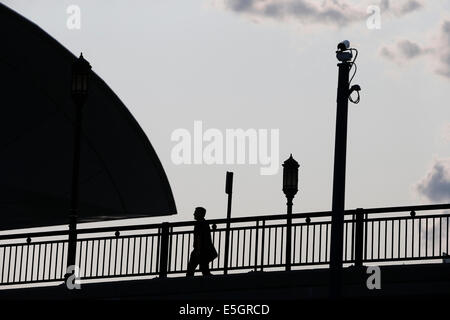 A pedestrian in silhouette walks under a pole mounted surveillance camera. Boston, Massachusetts, USA Stock Photo