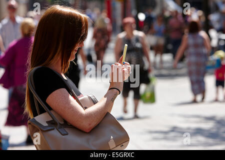 woman using smartphone to take a photo or text in Belfast city centre Stock Photo