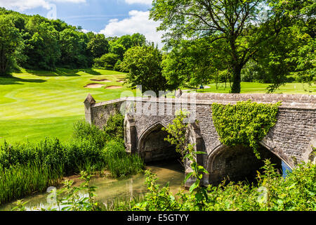A stone footbridge over the River By Brook with a golf course beyond. Stock Photo