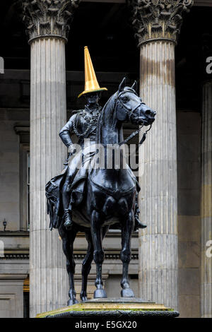 Glasgow, Scotland, UK. 31st July, 2014. In celebration of the success of the Commonwealth Games, the regular and iconic red and white traffic cone on the head of the Duke of Wellington statue (normally put there as a student prank) has been replaced by one painted gold. The statue, with a traffic cone on top, outside the Gallery of Modern Art in Royal Exchange Square has been used as an example of Glaswegian humour and is a continuing interest to tourists and locals alike. Credit:  Findlay/Alamy Live News Stock Photo