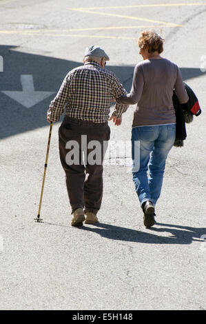 Old man with his walking stick helped by a younger woman in the street. Intergenerational complicity between old and young Stock Photo