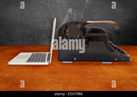 Modern silver laptop and an old black typewriter on a wooden table Stock Photo