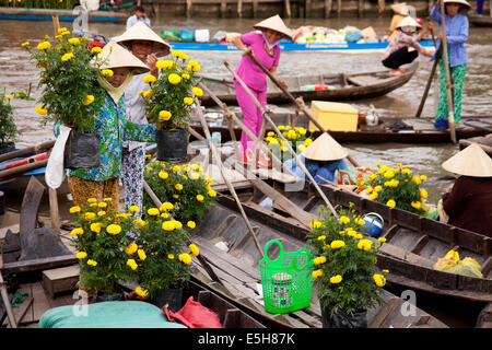Women wearing conical hats unload yellow flowers from a boat in the floating market in Soc Trang, a town in the Mekong Delta. Stock Photo