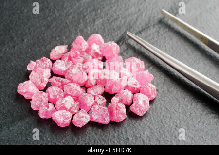 Pile of raw and uncut red and pink rybies or sapphires on black stone with tweezers at side. Stock Photo