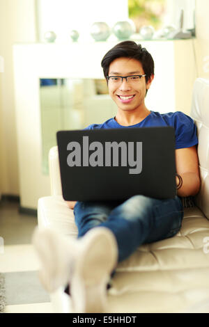 Young happy asian man lying on the sofa with laptop at home Stock Photo