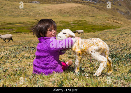 A little girl of the Quechua Indians sitting on a mountain meadow and holding a newborn lamb in her arms, Cordillera Huayhuash Stock Photo
