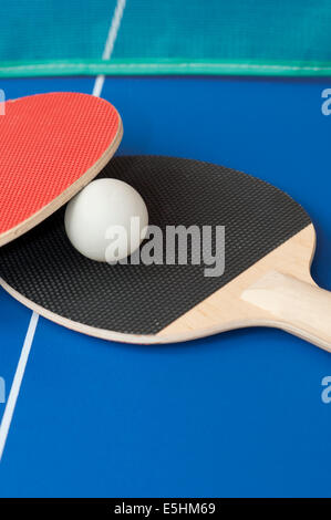 red and black table tennis bats on a blue table with green net in background Stock Photo