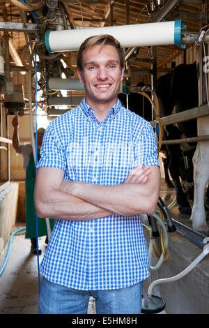 Portrait Of Dairy Farmer In Milking Shed With Cows Stock Photo