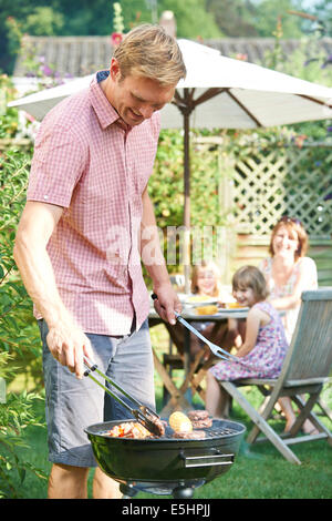 Father Cooking Barbeque For Family In Garden At Home Stock Photo